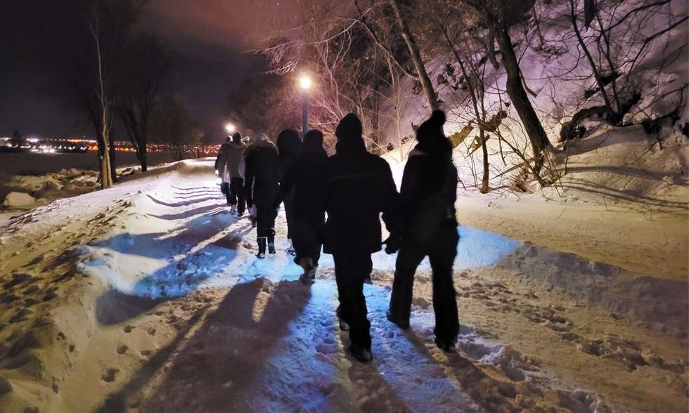 Un groupe de personnes en randonn\u00e9e sur un sentier enneig\u00e9 en soir\u00e9e.