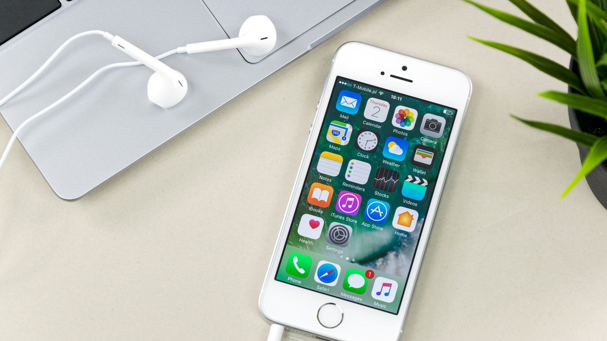 Un iPhone avec des écouteurs est placé à côté d'un ordinateur Apple et d'une plante verte.