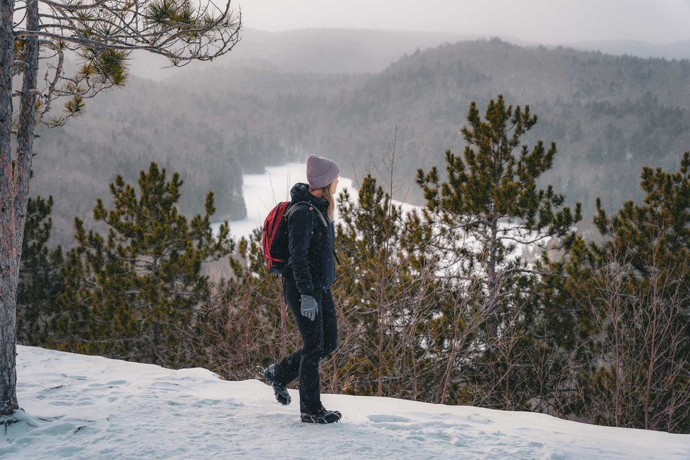 Un\u00b7e randonneur\u00b7euse marche sur un sentier enneig\u00e9 au-dessus d\u2019un lac gel\u00e9.