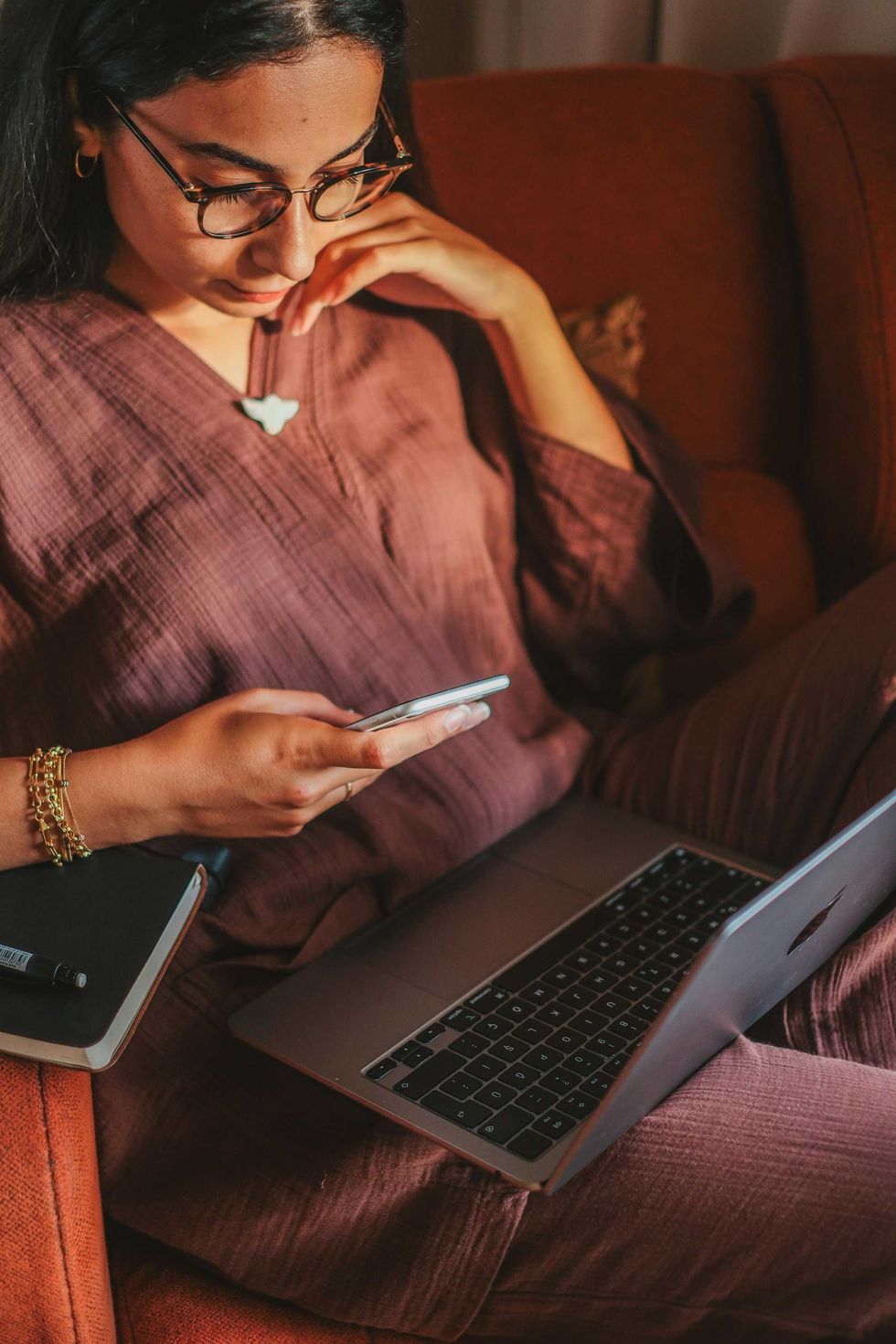 Une femme regarde son t\u00e9l\u00e9phone avec son ordinateur portable sur ses genoux.