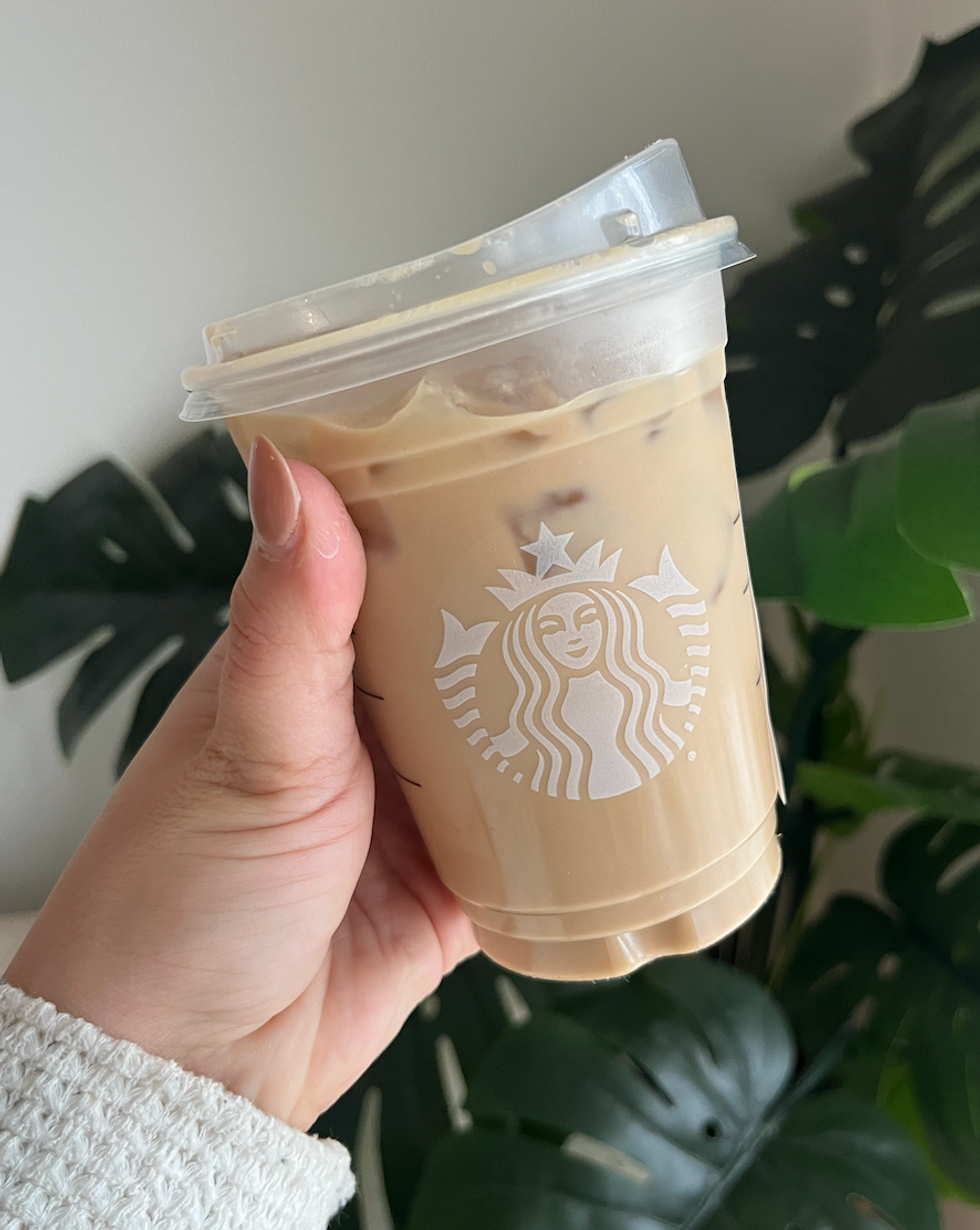 Une main qui tient un caf\u00e9 latte glac\u00e9 de chez Starbucks devant une plante.