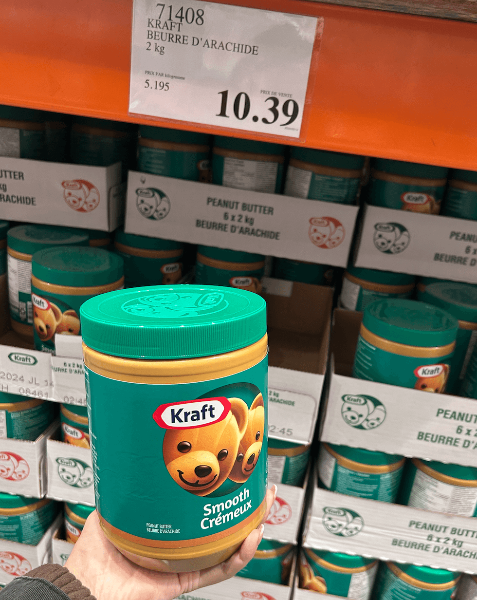 Une main tenant un contenant de beurre d'arachide son \u00e9talage du Costco.