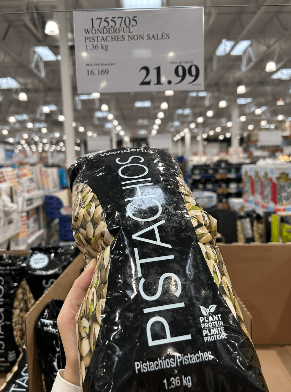 Une main tenant un sac de pistaches non sal\u00e9es Wonderful devant une \u00e9talage du Costco.