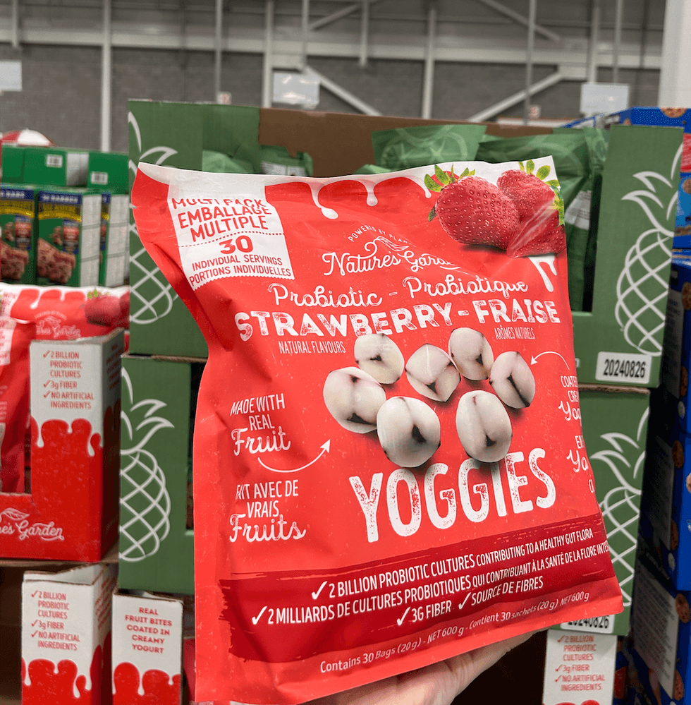 Une main tenant un sac de Yoggies probiotiques \u00e0 la fraise de Nature's Garden devant un \u00e9talage au Costco.
