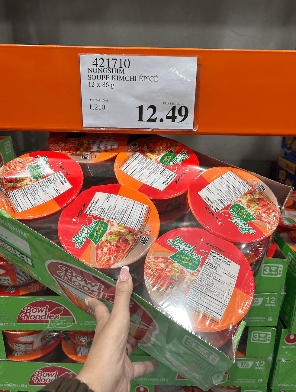 Une main tenant une boite contenant douze soupes au kimchi \u00e9pic\u00e9 devant son \u00e9talage au Costco.