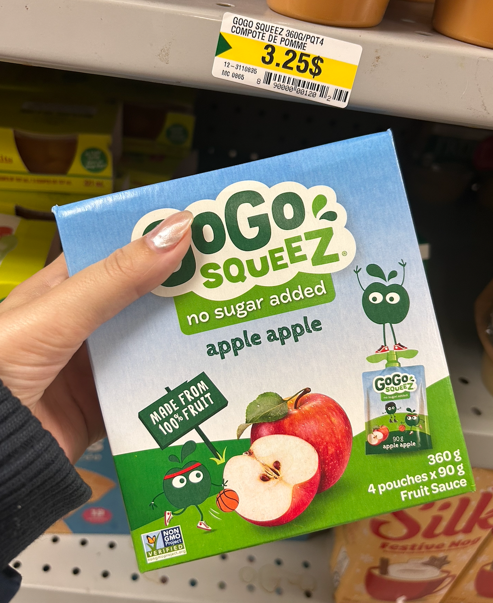 Une main tenant une boite de compote de fruits GoGo squeeZ au Dollarama.