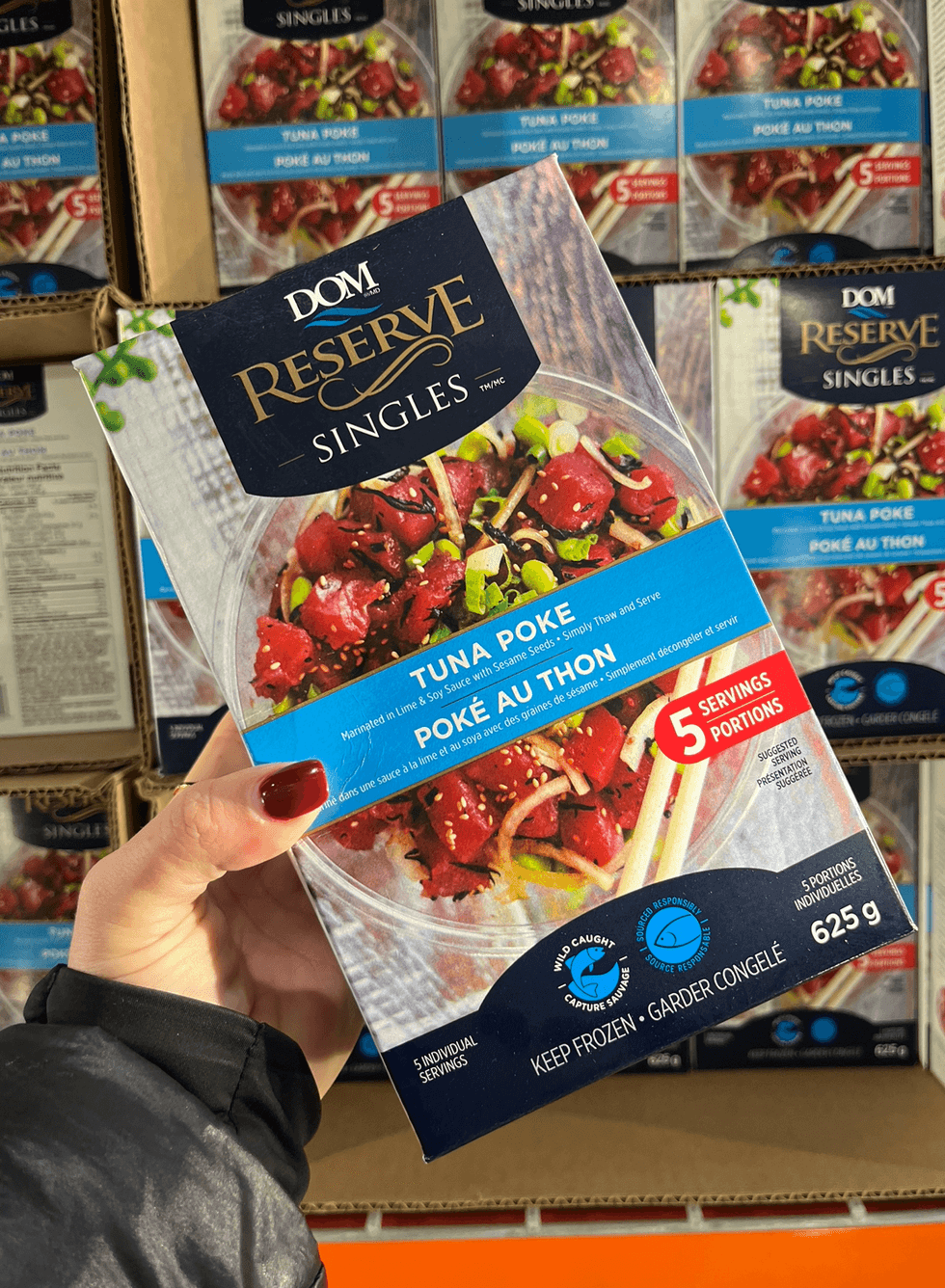 Une main tenant une boite de pok\u00e9 au thon DOM Reserve devant un \u00e9talage du Costco.