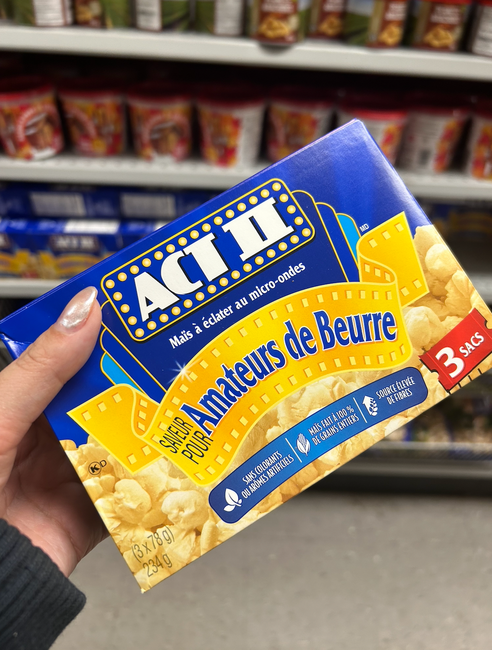 Une main tenant une boite de popcorn Act II au Dollarama.