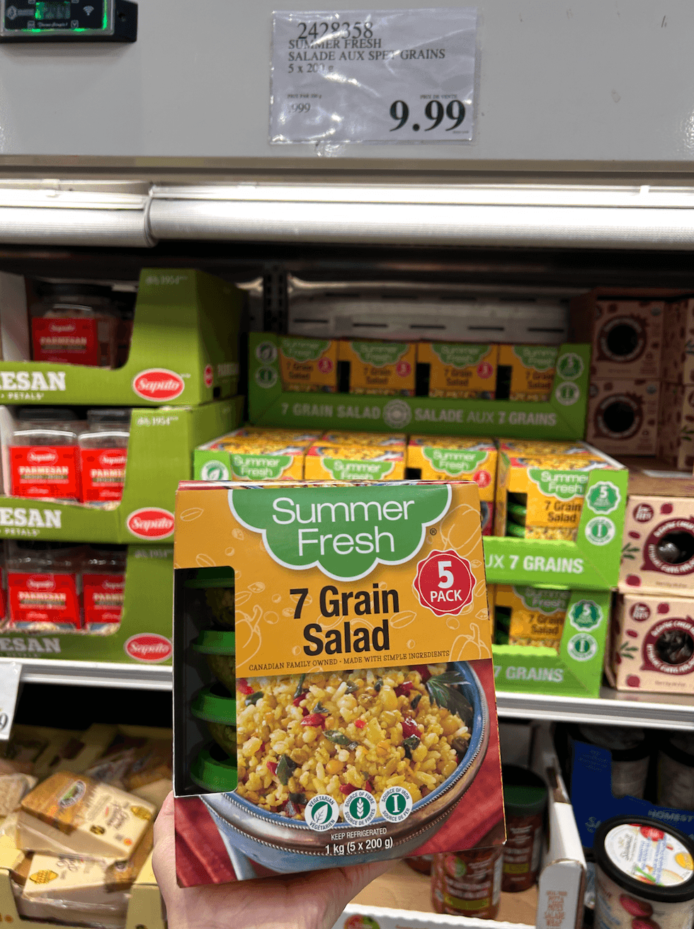 Une main tenant une boite de salades aux sept grains de Summer Fresh, devant un pr\u00e9sentoir r\u00e9frig\u00e9r\u00e9 du Costco.