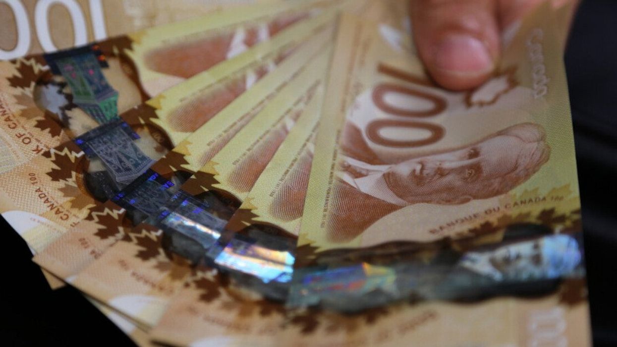 Une main tient des billets de 100 $ canadien placés en éventail.