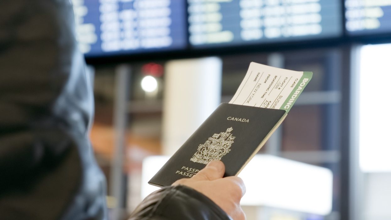 Une main tient un passeport canadien devant un tableau numérique dans un aéroport.