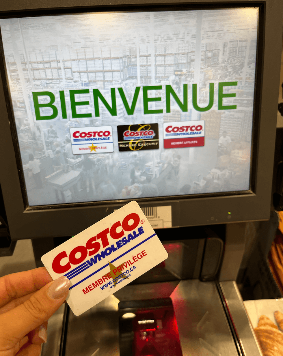 Une main tient une carte Costco \u00e0 la caisse libre service.