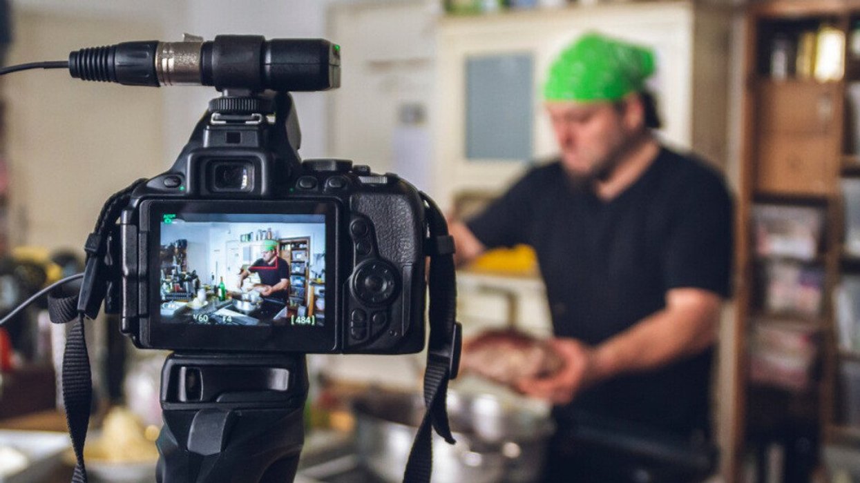 Une personne cuisine en arrière-plan pendant qu'une caméra enregistre en premier plan.