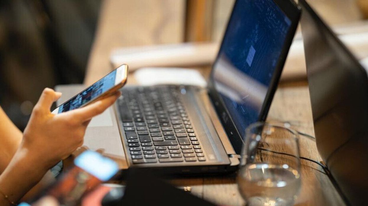 Une personne devant un portable avec un cellulaire dans une main.