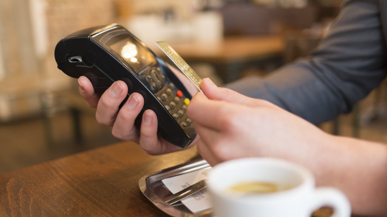 Une personne paye son café avec sa carte de crédit via un terminal de paiement.