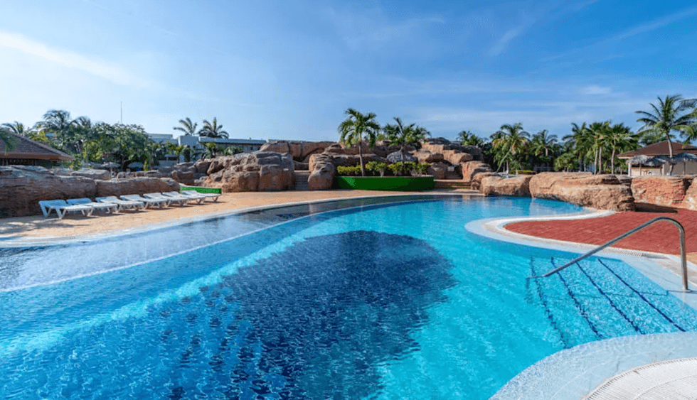 Une piscine de l'h\u00f4tel Grand Memories Varadero \u00e0 Cuba, entour\u00e9e de pierres, de palmiers et de chaises longues.