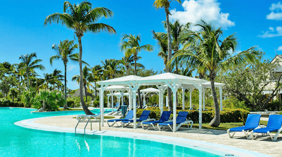 Une piscine de l'h\u00f4tel Memories Cayo Largo \u00e0 Cuba, entour\u00e9e de palmiers et de chaises longues bleues.