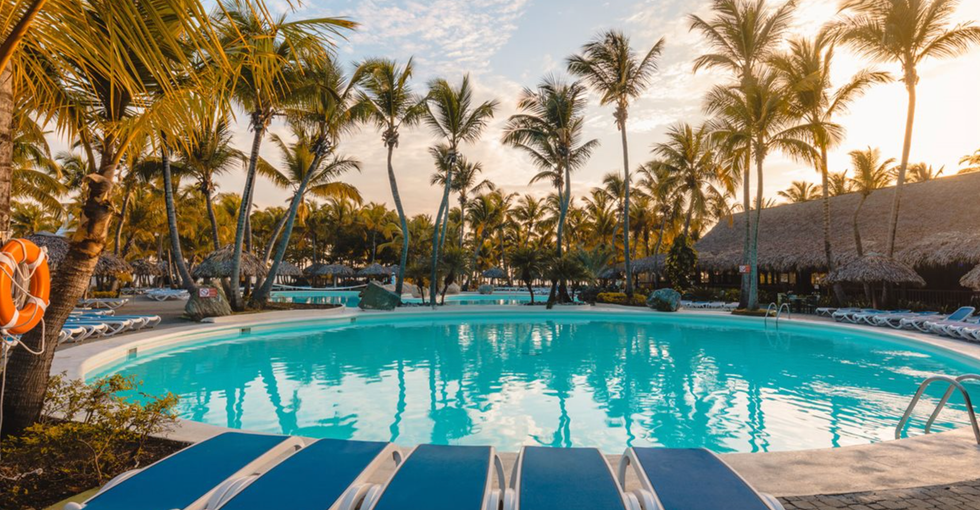 Une piscine entour\u00e9e de palmiers et de chaises longues bleues \u00e0 l'h\u00f4tel Playabachata Spa Resort \u00e0 Puerto Plata.