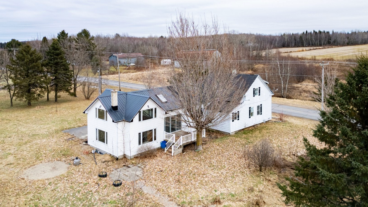 Vue aérienne d'une grande maison blanche et grise à vendre sur un terrain spacieux au Québec.