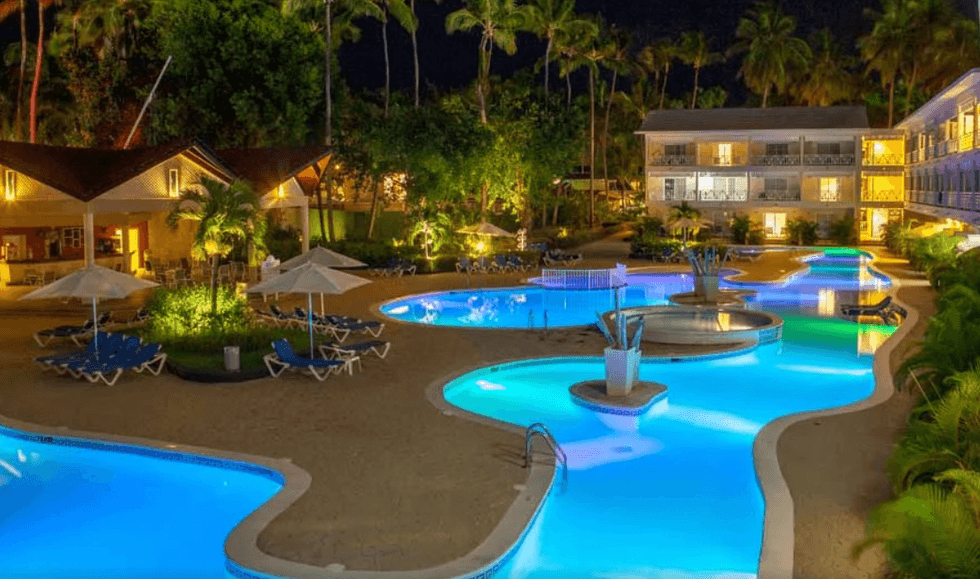 Vue nocturne d\u2019un complexe h\u00f4telier tropical avec plusieurs piscines aux formes arrondies illumin\u00e9es d\u2019un bleu vif.