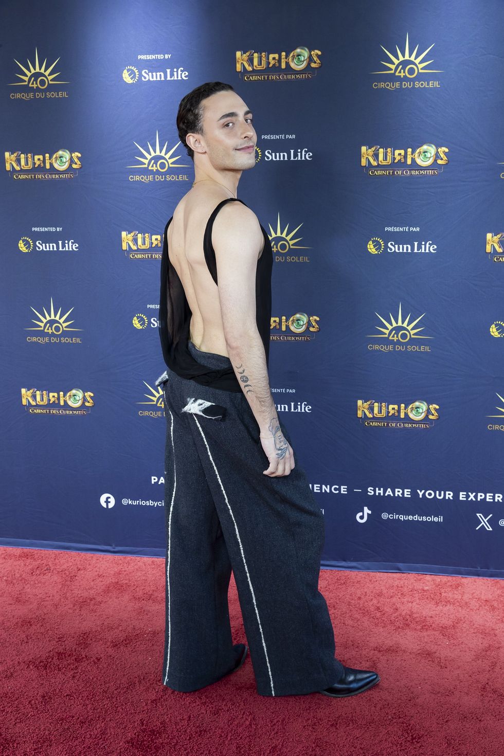 Zo\u00e9 Duval, v\u00eatu de noir, sur le tapis rouge de Kurios du Cirque du Soleil.